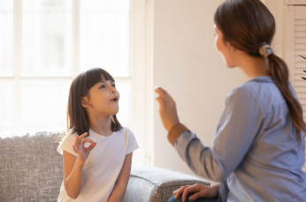 A mom and daughter learning sign language in their lounge